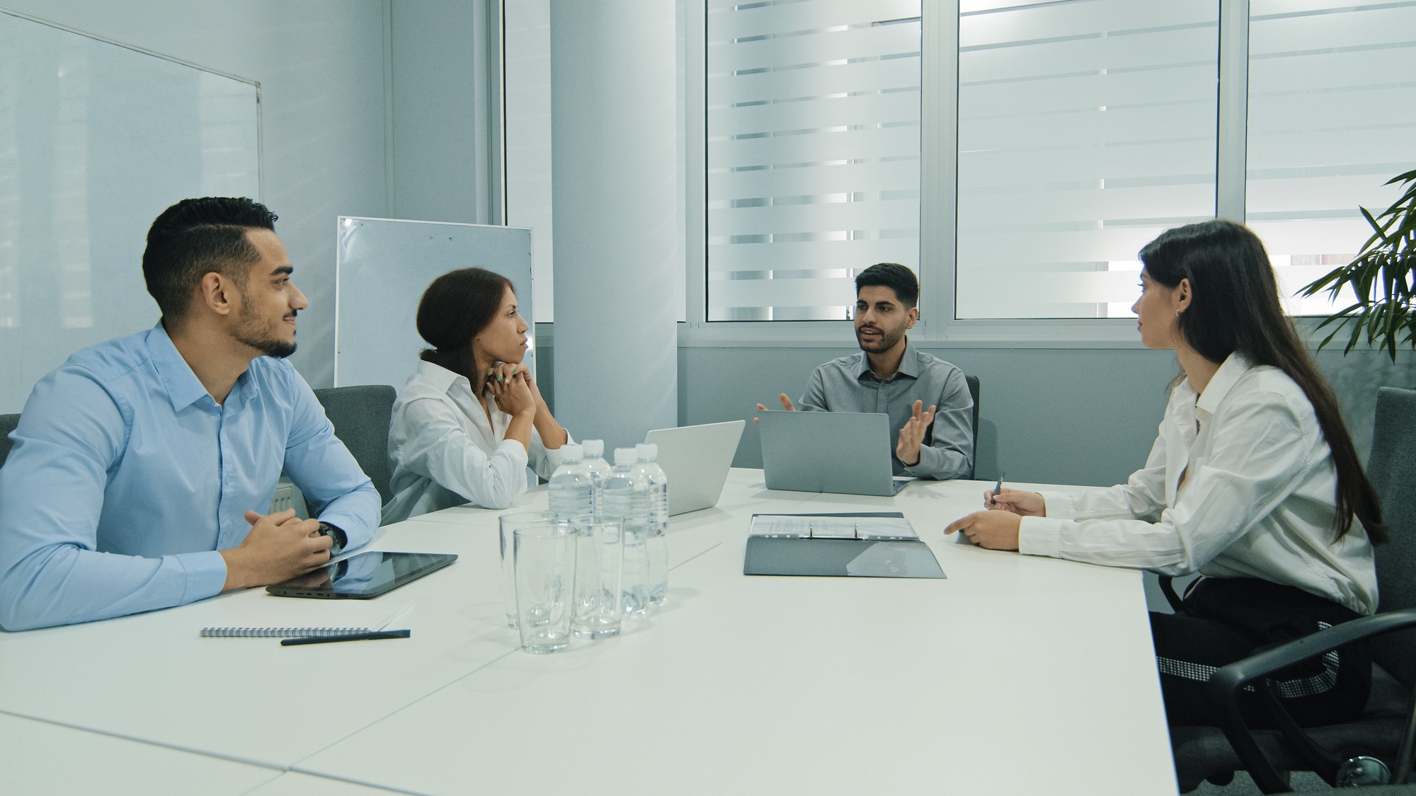 Young indian team leader sitting with colleagues, discussing issues at negotiations meeting. Skilled